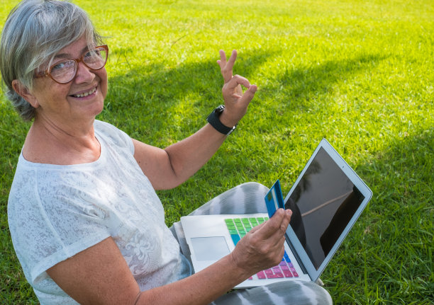 在公园里用笔记本电脑微笑的老年妇女
