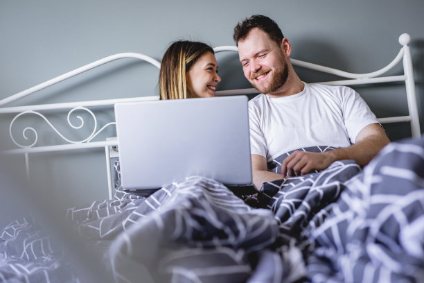 年轻夫妇在卧室的家里床上用电脑