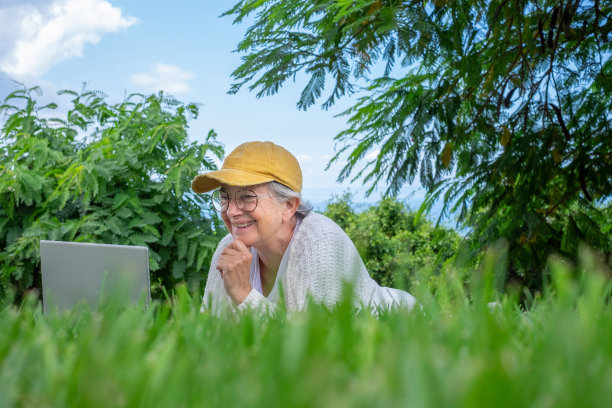 在公园里用笔记本电脑微笑的老年妇女
