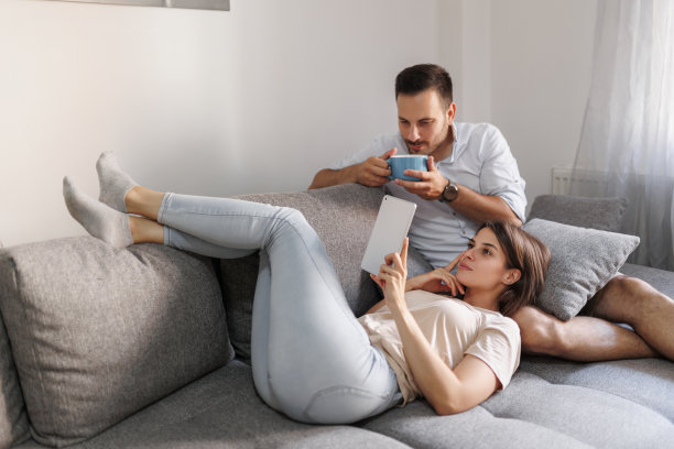 夫妇躺在家里的沙发上用平板电脑