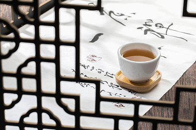 透过窗花的中国茶壶和茶杯在一幅书法画上富有禅意