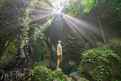 旅人站在热带雨林的洞穴里，仰望着从岩石上射下来的壮丽的阳光。人们旅行的奇妙欲望自然的概念