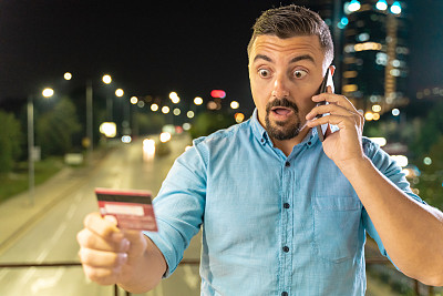 一个惊讶的男人用信用卡和智能手机进行网上购物