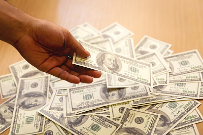 钱观百元美钞铺在木桌上，有人手里拿着钱付钱买东西或为腐败付钱。