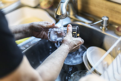 女人的手在不锈钢厨房水槽中清洗饮用玻璃