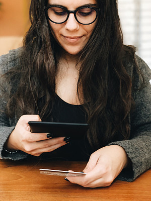 年轻女子用平板电脑扫描信用卡进行网上购物