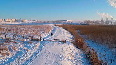 那个年轻的女人在白雪覆盖的乡村道路上奔跑和行走。低空无人机照片。