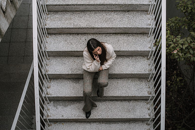 年轻女子拿着智能手机坐在楼梯上