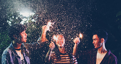 一群快乐的朋友与照明的火花和饮料在晚上享受在后院