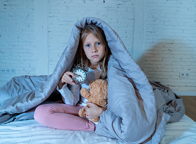 可爱的失眠小女孩坐在床上，看起来悲伤和疲惫，有睡眠问题，晚上睡不着觉，或者在儿童失眠焦虑睡眠障碍中过早醒来。