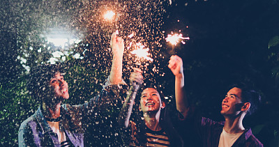 一群快乐的朋友与照明的火花和饮料在晚上享受在后院
