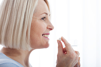 中年妇女握着玻璃杯、静水和药丸。患者口服止痛药或抗生素药丸，治疗慢性抑郁症或生物活性补充概念