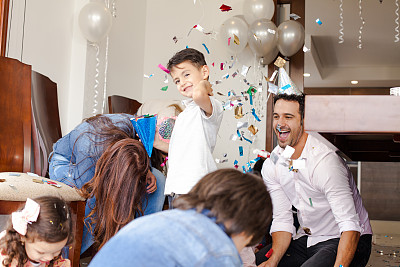 拉丁家庭庆祝其中一个孩子的生日。他出现在画面中央，看着镜头，被家人围绕着，家人向他扔五彩纸屑。