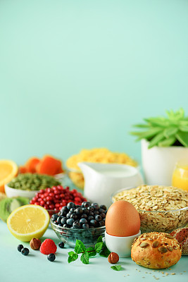 牛奶玉米片，新鲜浆果，酸奶，煮鸡蛋，坚果，水果，橙子，香蕉，桃子，蓝色背景的早餐。副本的空间。健康食品的概念。