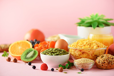 玉米片配牛奶，新鲜浆果，酸奶，煮鸡蛋，坚果，水果，橙子，香蕉，桃子作为早餐的黄色背景。副本的空间。健康食品的概念。
