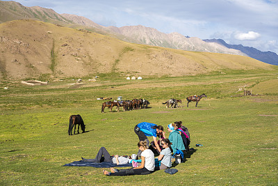 在吉尔吉斯斯坦的松科尔湖骑马一天后，游客们在营地休息，马在后面