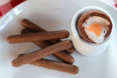 奶油/奶油蛋和巧克力手指饼干的形象在早餐桌上，蘸着甜奶油的复活节蛋黄和白色，红白格子桌布，甜点布丁糖果