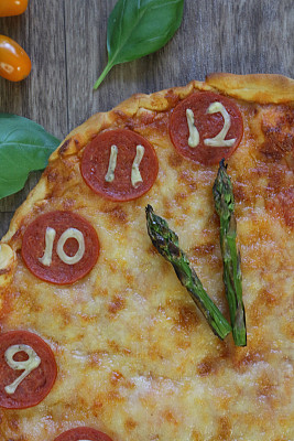 这是一个自制的披萨时钟，上面有意大利辣香肠切片、马苏里拉奶酪和芦笋作为时钟指针，告诉时间23:00 11点。这是意大利披萨餐厅为孩子们的生日派对食物而制作的儿童披萨时钟