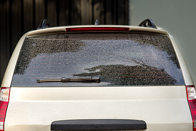 一辆脏车的后视图，一辆带有灰尘的后备箱盖和一个有缺陷的汽车雨刷的掀背车。