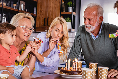 几代同堂的家庭庆祝生日，并在蛋糕上吹生日蜡烛