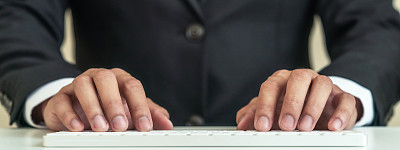 穿着黑色西装的商人双手合在一起敲击无线白色键盘。商务亚洲人的头在电脑上写电子邮件在经理，行政人员或专业法律人士的概念。