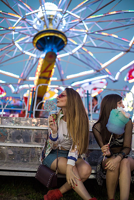 两个女性朋友玩棉花糖和棒棒糖在游乐园