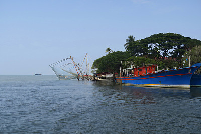 在印度南部喀拉拉邦科钦的科钦堡海滩，中国的渔网和拖网渔船在晴朗的蓝天下，在阿拉伯海科钦港的水域捕捞金枪鱼鲭鱼，Cheena vala中国渔网科钦的照片