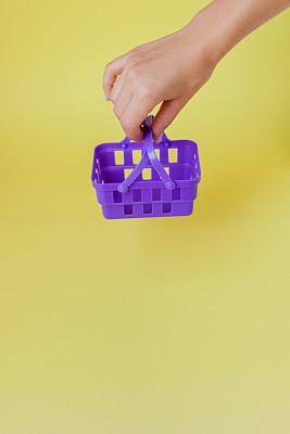 在市场商店买东西的概念。女人手拿着小购物篮手推车在趋势黄色的背景。