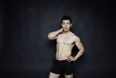 一名男子/一人/腰部以上/正面20-29岁英俊的中国人/东亚民族男性站在黑色背景前，穿着纽扣衬衫/衬衫/内衣/男式内裤/半裙