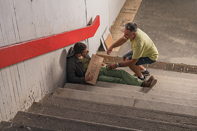 绝望的乞丐正在接受城市地下的一个男人给的钱和支持
