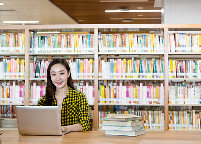 在图书馆里用笔记本电脑和书学习的女人