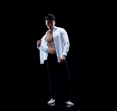 中国民族年轻男性脱衣舞娘站在黑色背景穿着纽扣衬衫
