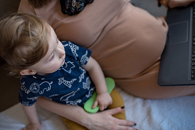 孕妇使用笔记本电脑，照顾她的小儿子