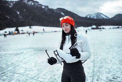 一名女子站在结冰的湖面上，将冰鞋的护刃重新穿上