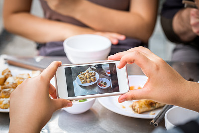 一名女子在户外餐厅用智能手机为越南餐拍照