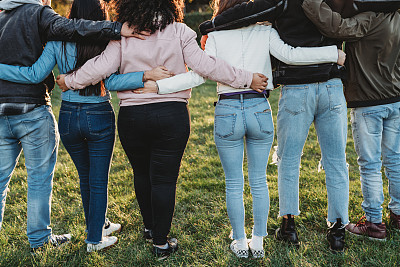 六个青少年朋友在公园里拥抱在一起，后视图