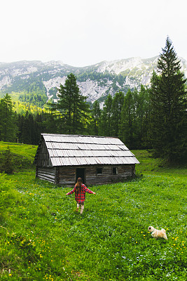 一个年轻的女人和一只狗在朱利安阿尔卑斯山的老木屋附近美丽的草地上感觉自由奔跑