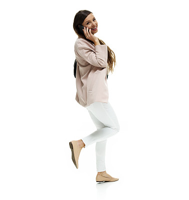 白人年轻女性穿着夹克，拿着钱包，用手机在白色背景前行走