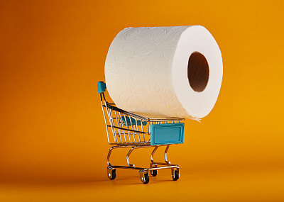 超市购物车里有一卷巨大的卫生纸，背景是鲜艳的黄色/橙色