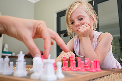 小女孩看着她的妈妈在他们的棋局中走一步棋