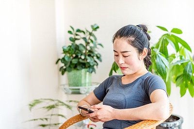 在客厅里使用智能手机的亚洲年轻女子