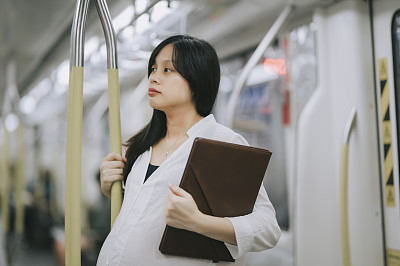 a pregnant asian chinese businesswoman on the move taking public transportation commuter monorail in kuala lumpur to work with her digital tablet business on the move