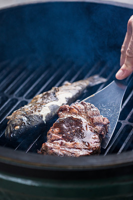 男人的手翻着烤肉上的牛排和鱼。用抹刀