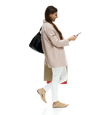 白人女性穿着夹克，拿着钱包，用手机走在白色背景前