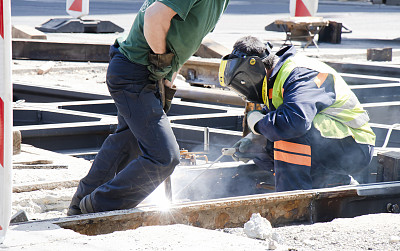 焊接工在城市街道十字路口工作，用新铁轨替换旧铁轨并进行电弧焊接