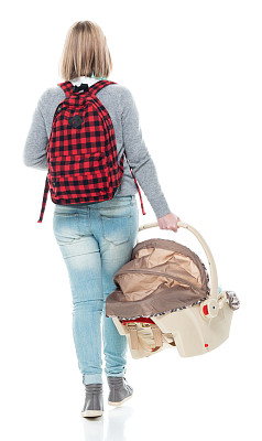 z一代婴儿-人类年龄的初中生走路背着背包，抱着汽车安全座椅和使用耳机