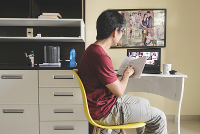 一名男子在家里参加一个视频会议，与在线图书俱乐部的成员一起阅读