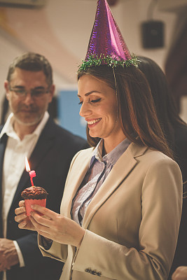 快乐的女商人戴着派对帽拿着蛋糕和生日蜡烛