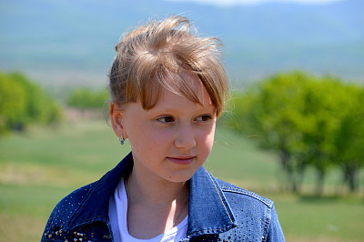 肖像10岁的俄罗斯金发女孩微笑在绿色的田野背景。可爱的脸，看着别处