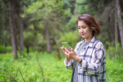 年轻的亚洲女子在森林里戴着耳机听音乐